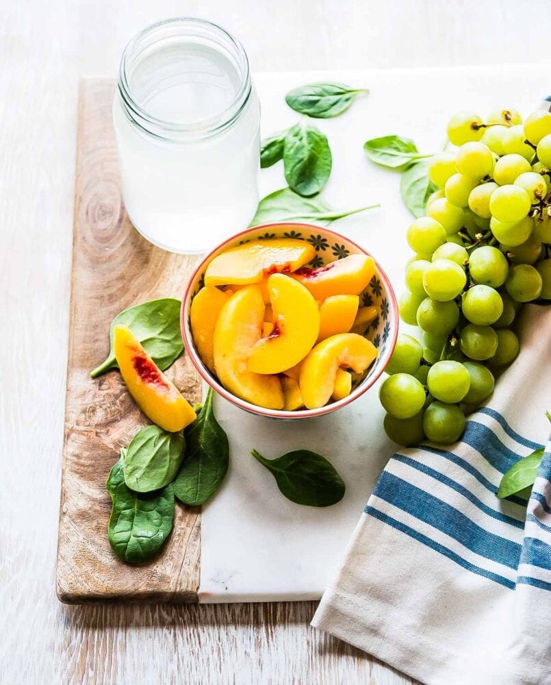 ingredients for a peach spinach smoothie including green grapes, peaches, spinach and coconut water.