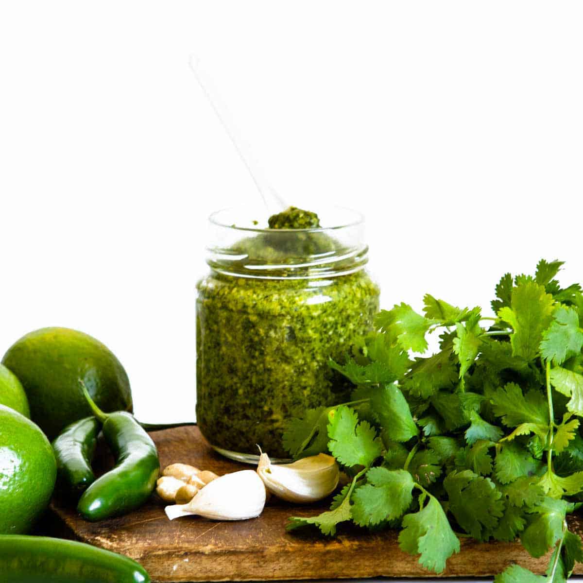 cilantro pesto in glass jar surrounded by limes, garlic, cilantro and serrano pepper.