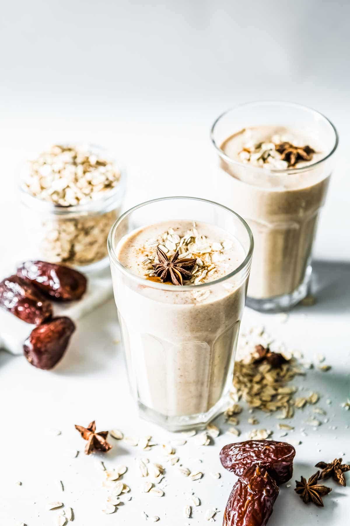 Side angle of CInnamon Date Smoothie in tall glass cups with medjool dates on the side.
