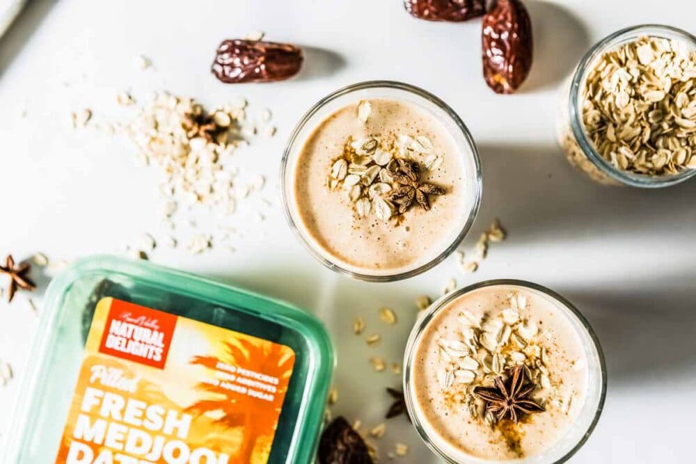 Two Date Smoothies made with Medjool dates, rolled oats, and cinnamon, served in glasses topped with star anise and surrounded by ingredients.