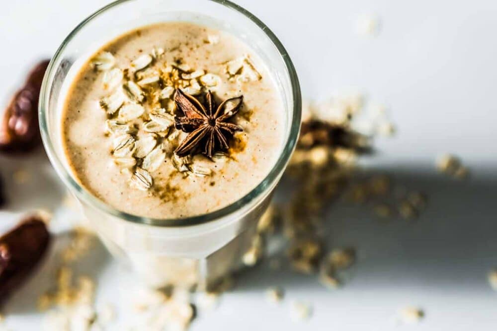 Top view of cinnamon date smoothie with rolled oats sprinkled on top and on the countertop.