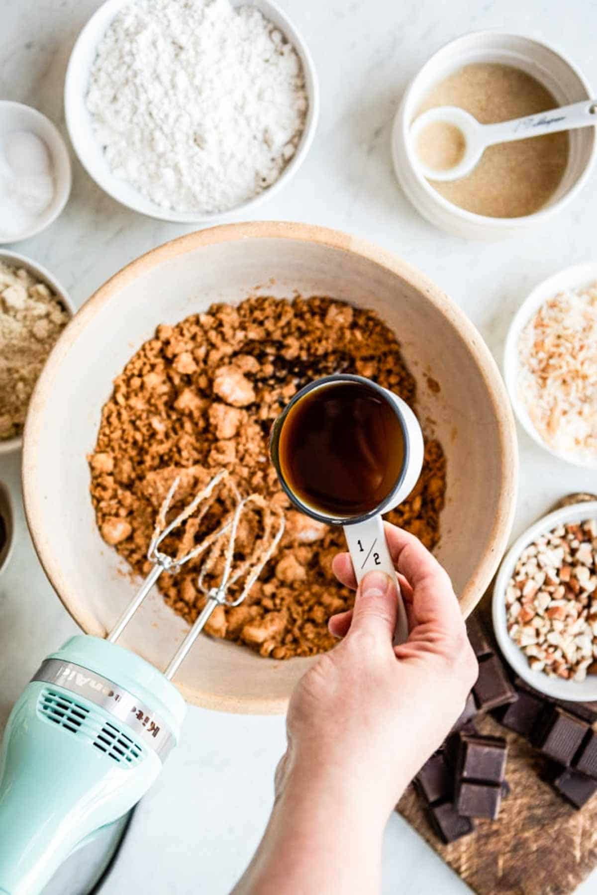 pouring maple syrup into a bowl of mixed ingredients.