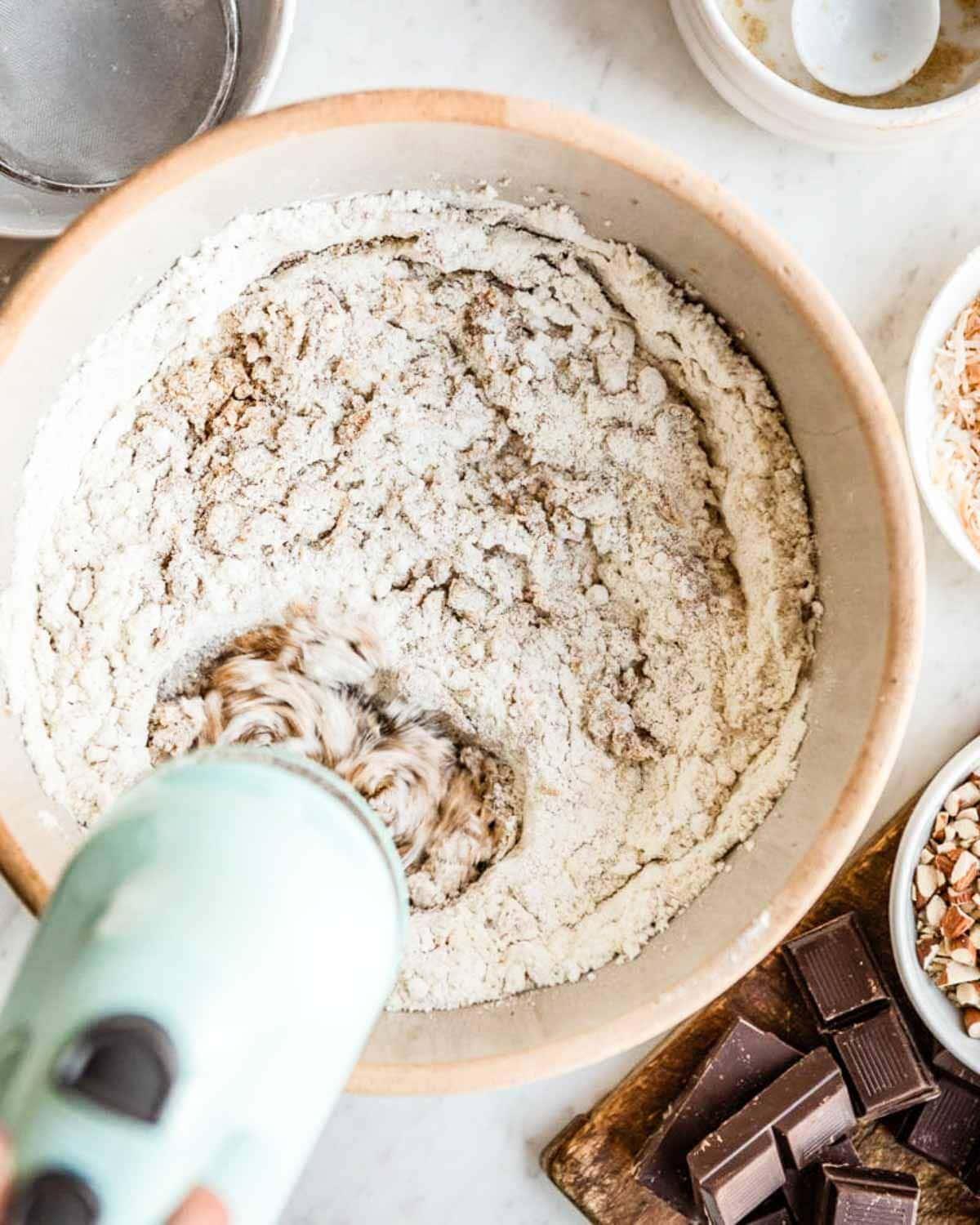 using a blue hand mixer to beat ingredients in a large bowl.