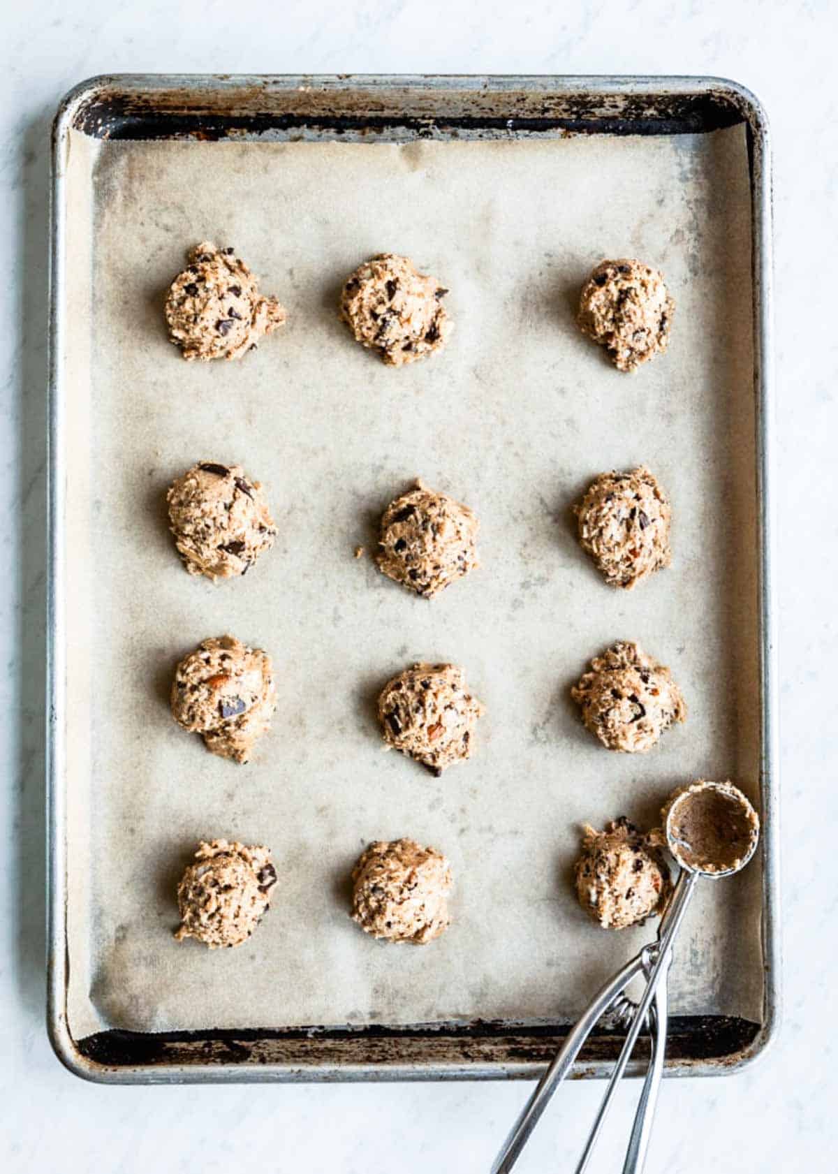 vegan chocolate chip cookies with a cookie scoop onto a parchment lined baking sheet.