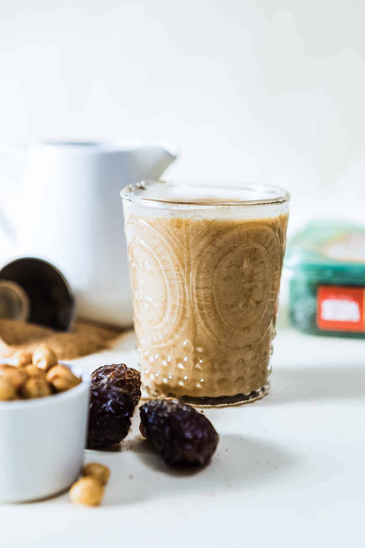 Healthy caramel protein shake in a festive etched glass next to a bowl of cashews and some pitted medjool dates.