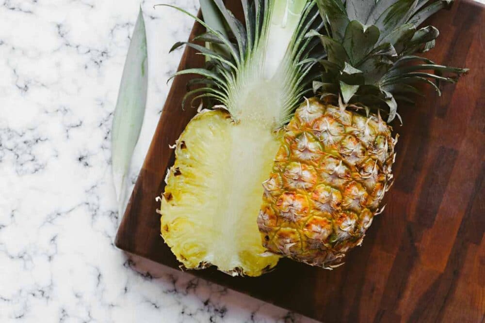 fresh pineapple sliced in half on a wooden cutting board.