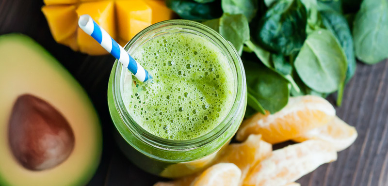 Close up of a green smoothie in a mason jar with a blue paper straw.