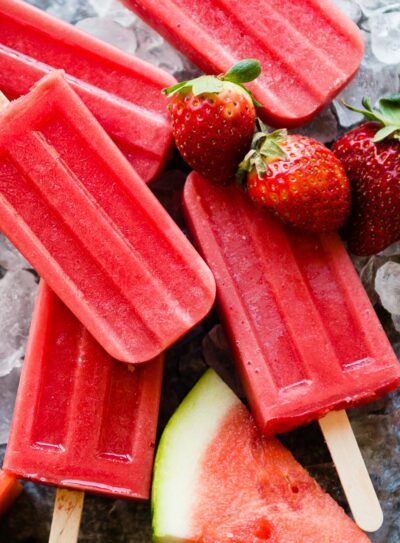 5 bright red popsicles surrounded by fruit and ice.