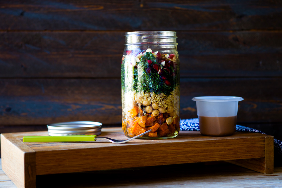 a fully layered mason jar salad with a homemade dressing next to it, ready to go