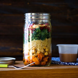 a fully layered mason jar salad with a homemade dressing next to it, ready to go