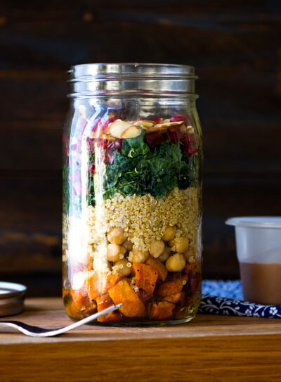 a fully layered mason jar salad with a homemade dressing next to it, ready to go