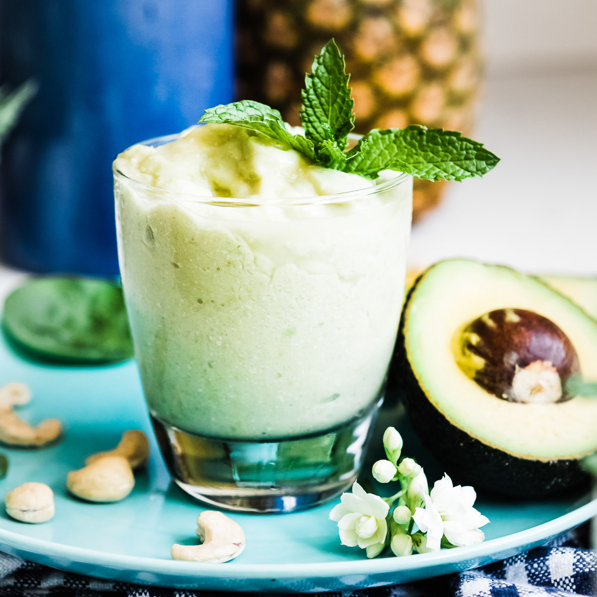 Creamy avocado smoothie recipe served in a glass, alongside a plate with a half avocado.