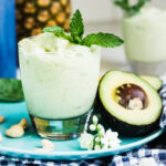 Creamy avocado smoothie recipe served in a glass, alongside a plate with a half avocado.