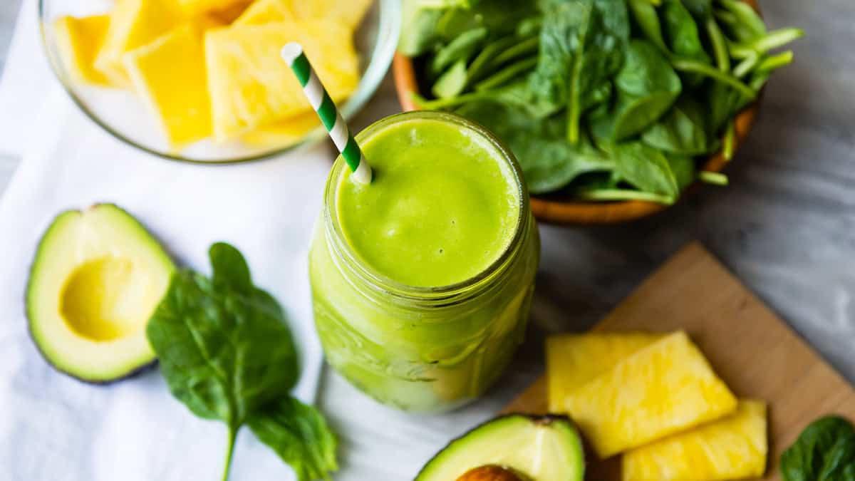 Healthy green smoothie with spinach, avocado, and pineapple on a wooden board.