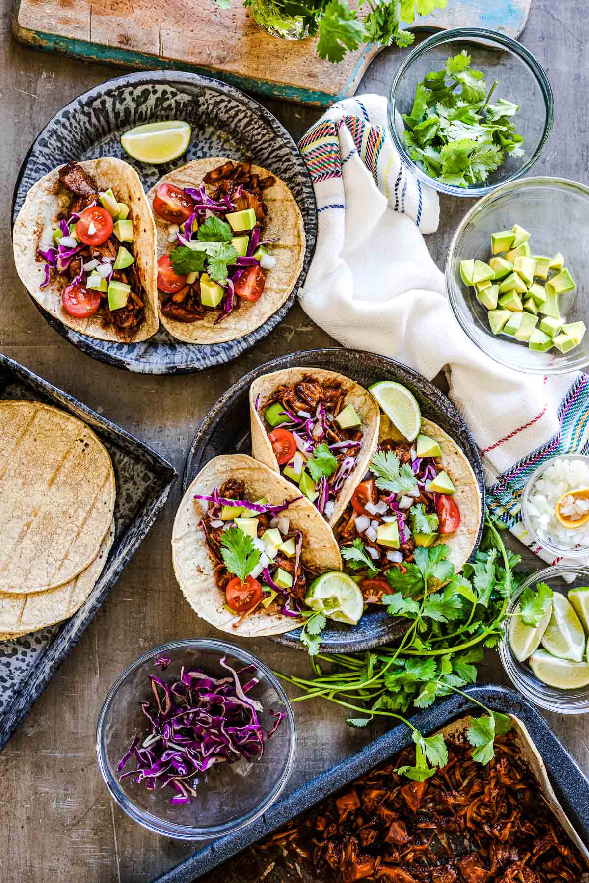 jackfruit tacos on plates with purple cabbage in a bowl.