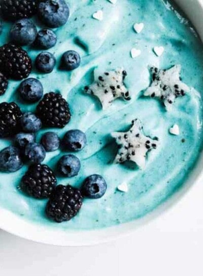 banana nice cream turned blue with spirulina powder in a white bowl topped with fresh fruit and white sprinkles.