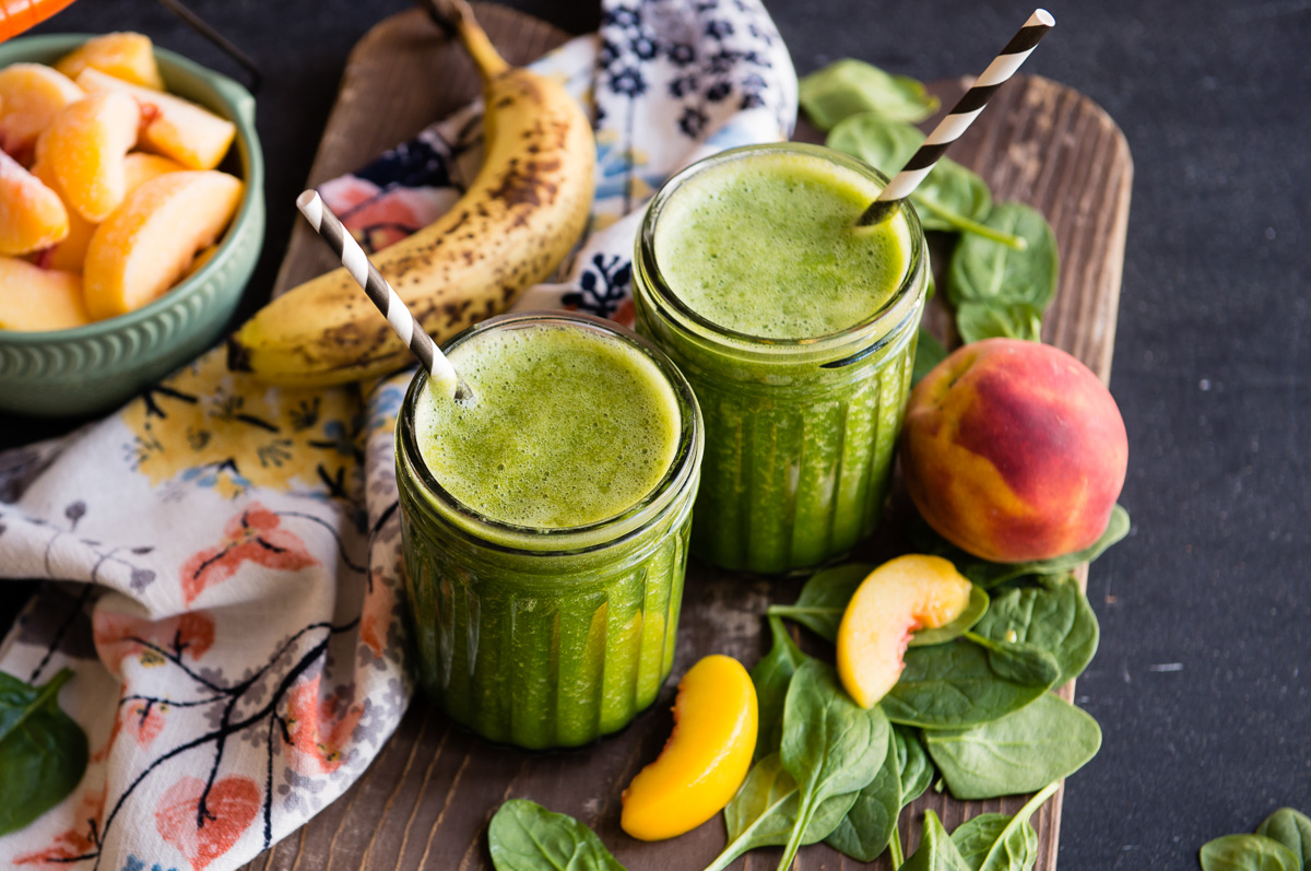 Two glass jars of banana peach smoothie with peach slices and paper straws.
