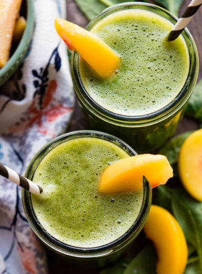 Two glass jars of banana peach smoothie with peach slices and paper straws.