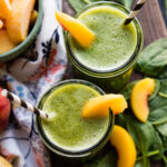 Two glass jars of banana peach smoothie with peach slices and paper straws.