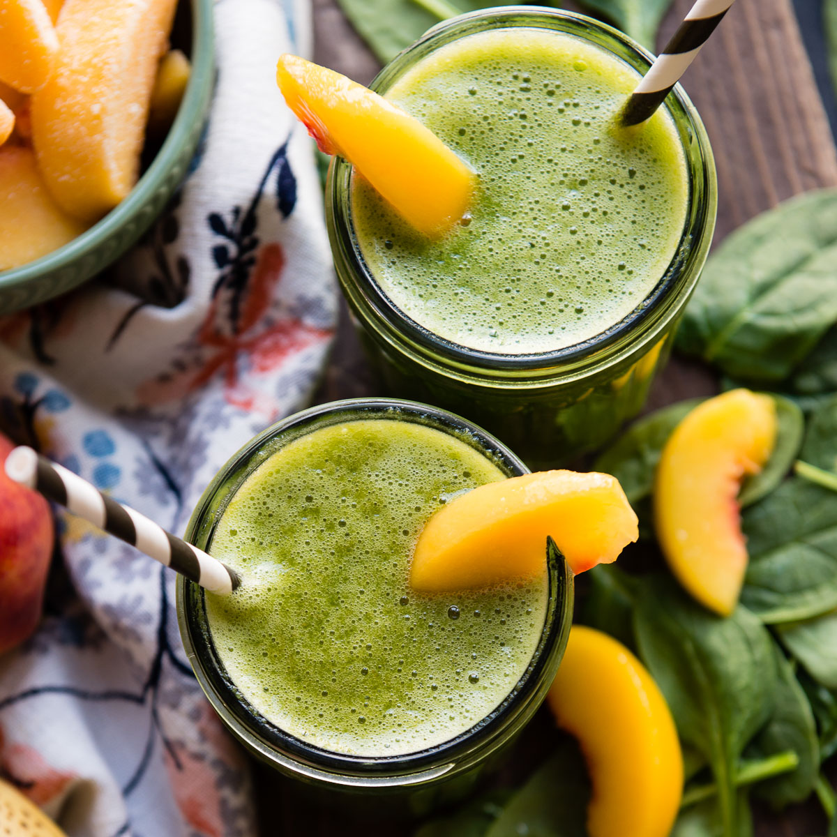 Two glass jars of banana peach smoothie with peach slices and paper straws.