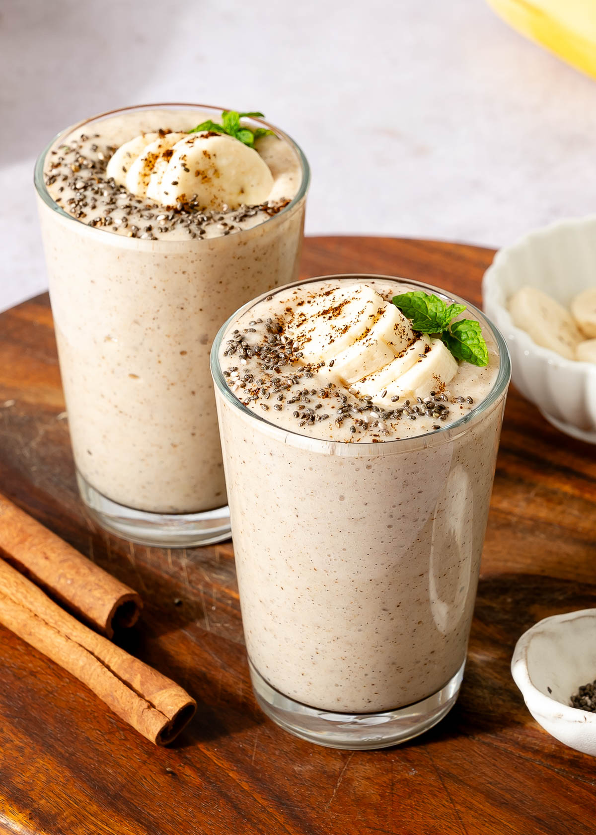 Two glass of banana protein shake with banana slices and chia seeds on top