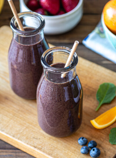 Two glasses of berries citrus smoothie surrounded by fresh ingredients.