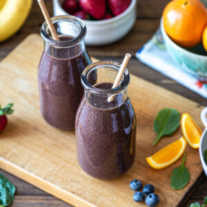 Two glasses of berries citrus smoothie surrounded by fresh ingredients.