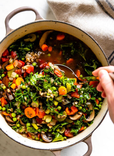 Hand ladling out a scoop of vegetable barley soup