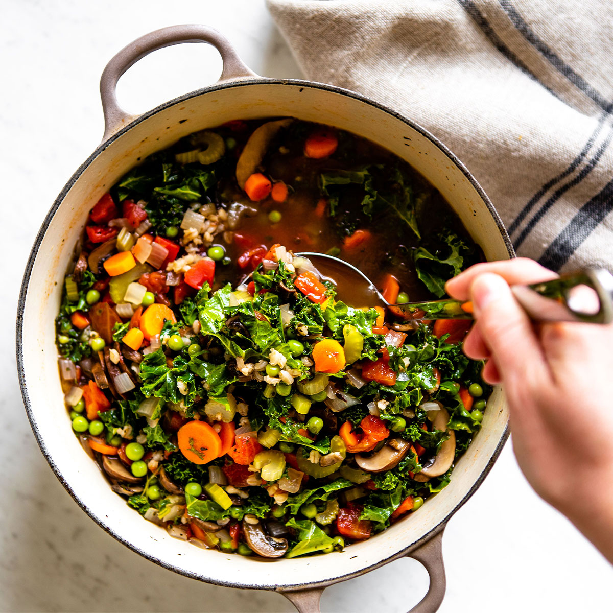 Hand ladling out a scoop of vegetable barley soup