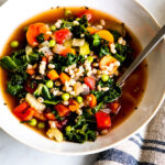 A white bowl filled with vegetable barley soup ready to be enjoyed.