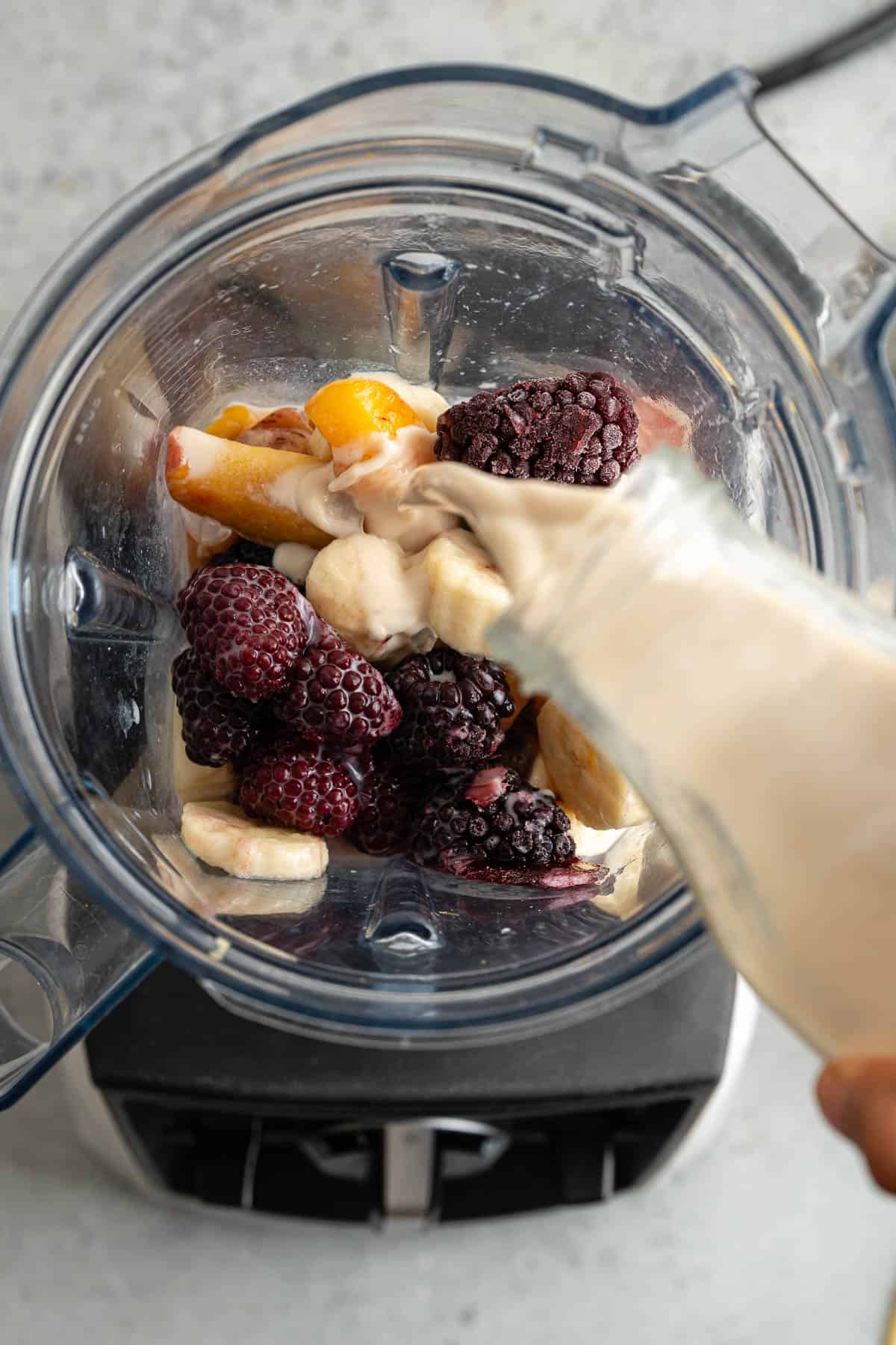 Pouring almond milk over blackberry peach smoothie ingredients