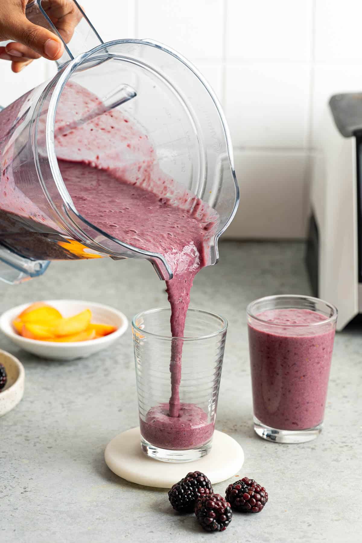Pouring blackberry peach smoothie in a glass