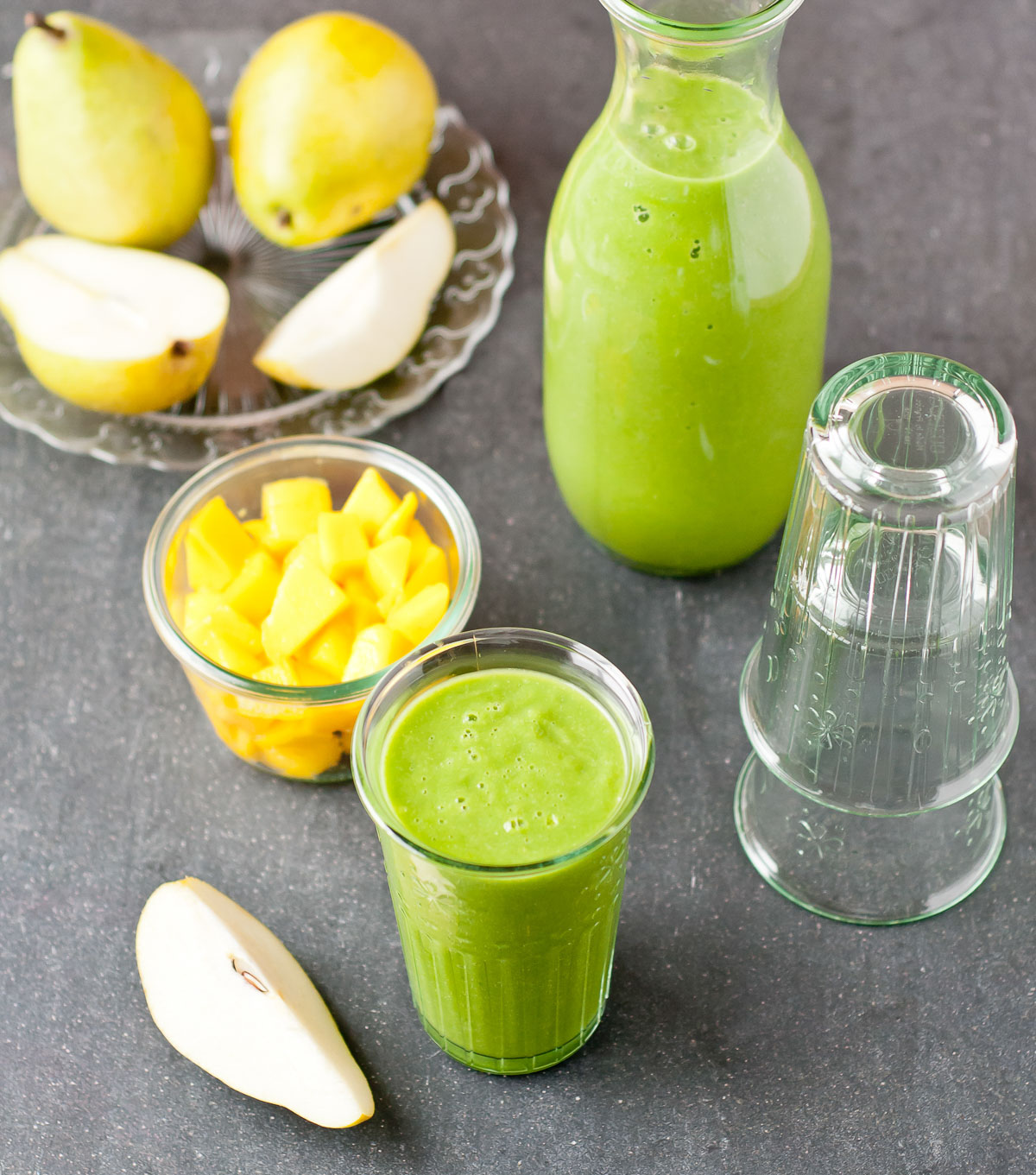 a tall glass of brain food smoothie along side sliced pears and mango.