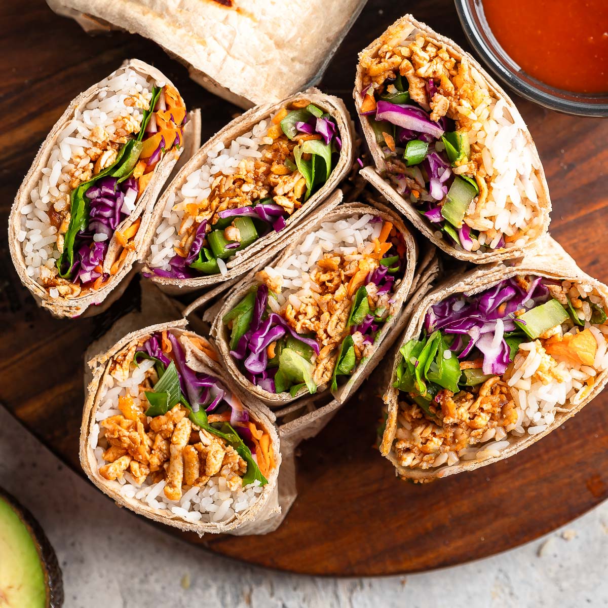 Wraps cut in half on plate with cabbage, tofu, rice and avocado.