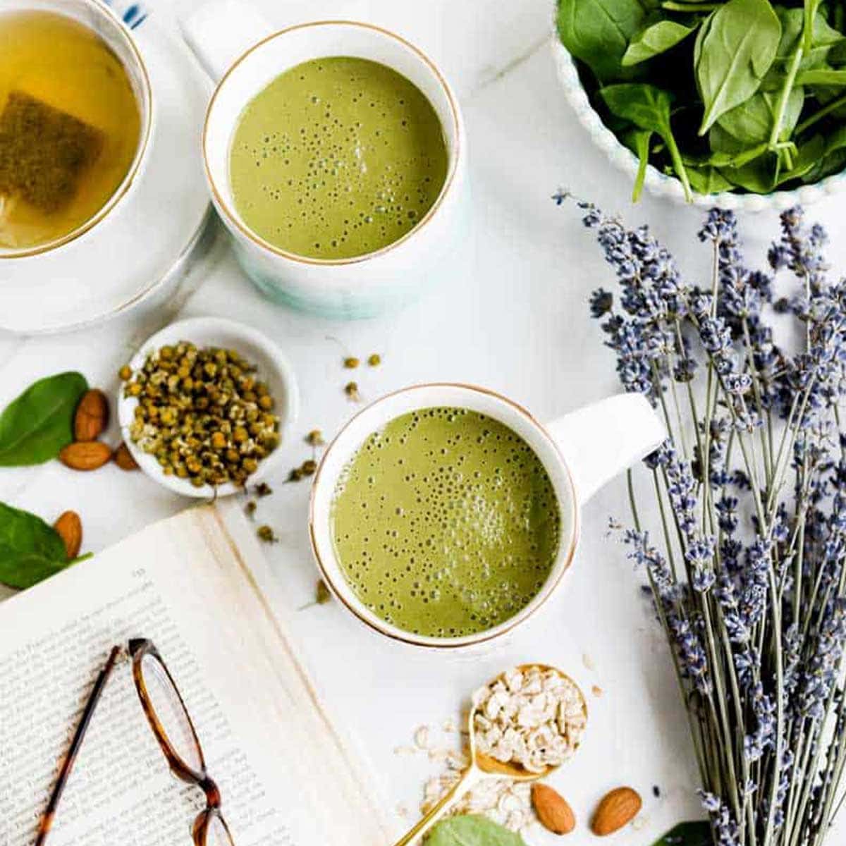 green bedtime smoothie in white mug surrounded by foods that help you sleep like lavender, almonds and spinach.