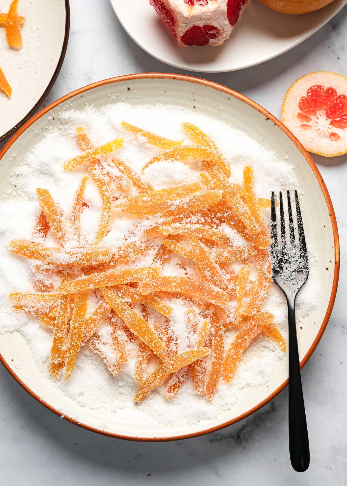 Candied grapefruit peel strips being rolled in granulated sugar