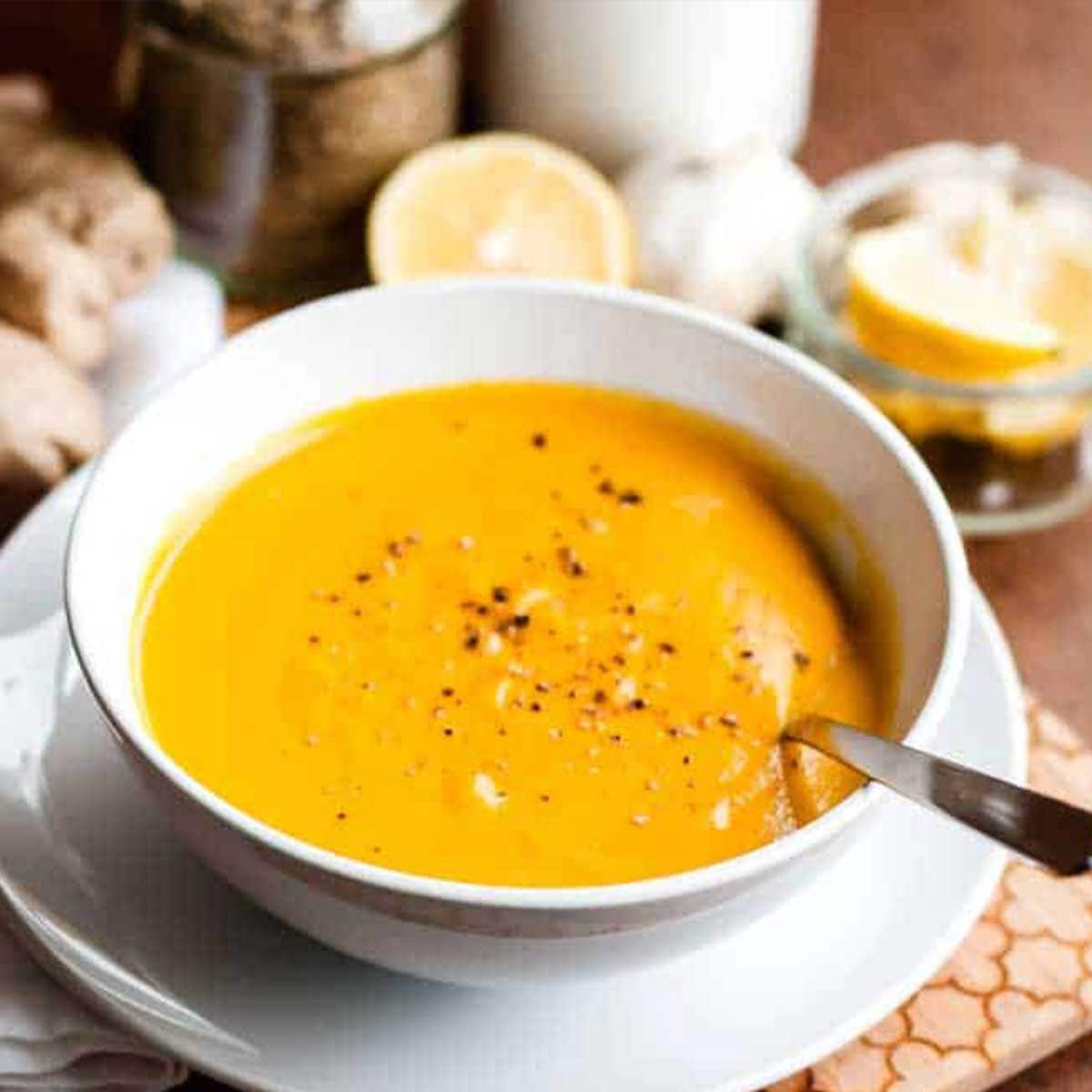 carrot ginger soup recipe in a white bowl with a stainless steel spoon and cracked black pepper on top.