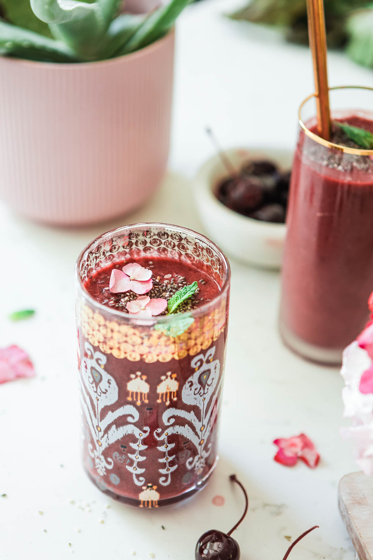 Glass of cherry beet smoothie garnished with flower petals, chia seeds, and mint leaves. 