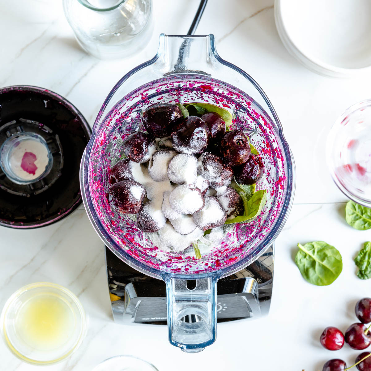 Top-down view of a blender container with spinach, cherries, and collagen powder.