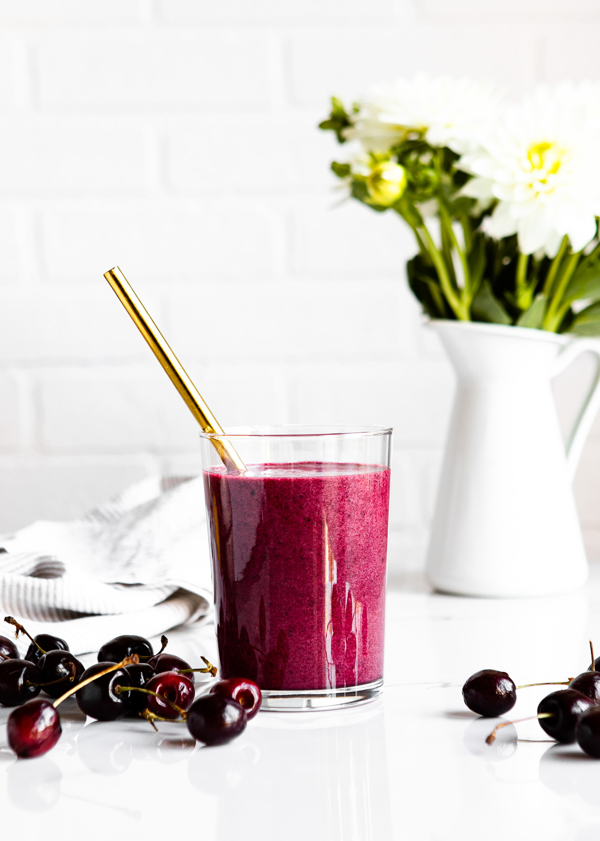 A vibrant cherry collagen smoothie with fresh scattered cherries and a gold straw, ready to be enjoyed.