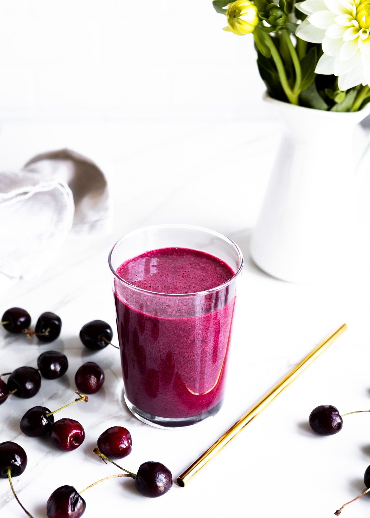 A vibrant cherry collagen smoothie with fresh scattered cherries and a gold straw.