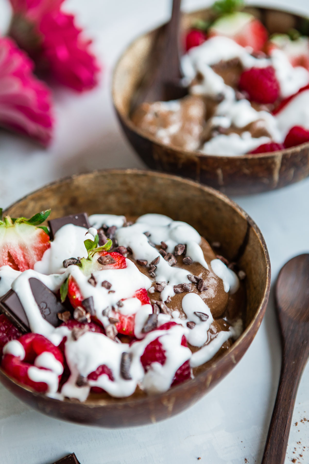 Two chocolate smoothie bowls, topped with coconut whipped cream and fresh berries.