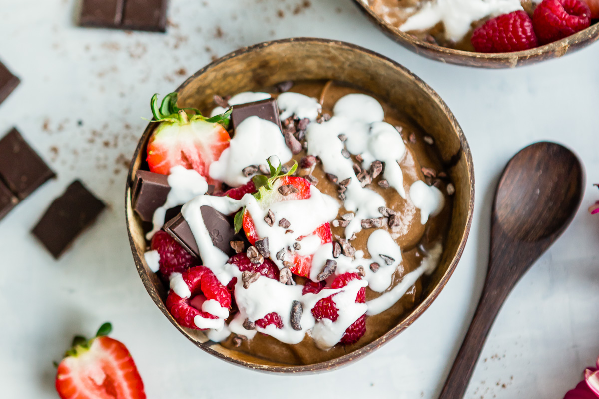 A chocolate smoothie bowls, topped with coconut whipped cream and fresh berries.