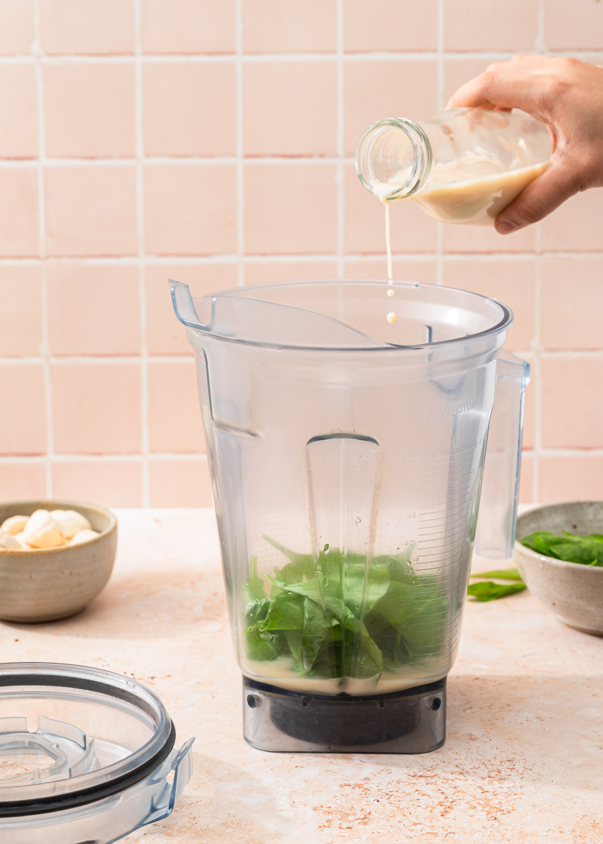 Almond milk being poured into a blender with spinach.