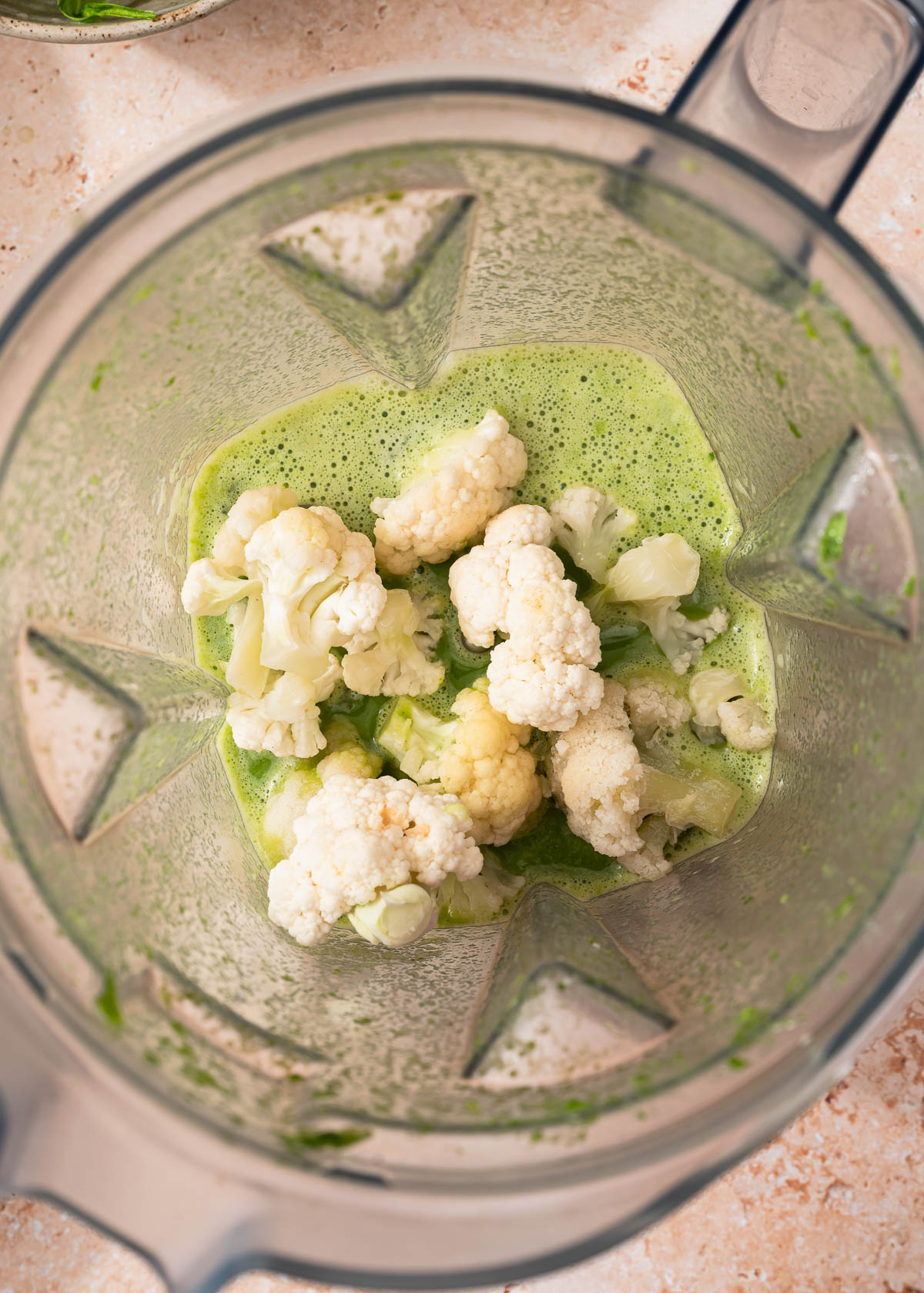 Cauliflower florets added to blender with already blended spinach and almond milk.