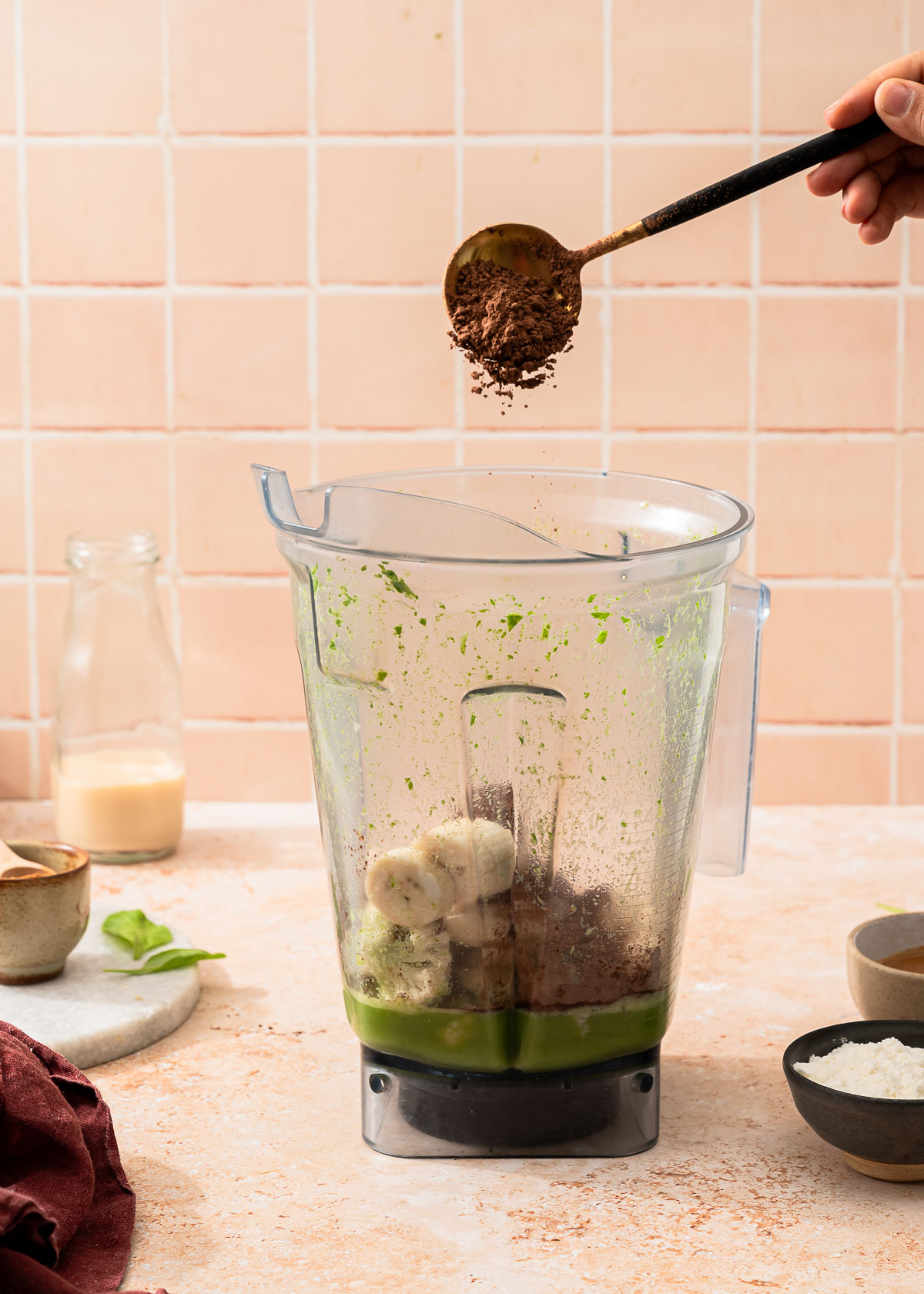 Cocoa powder being poured from a scoop into a blender container