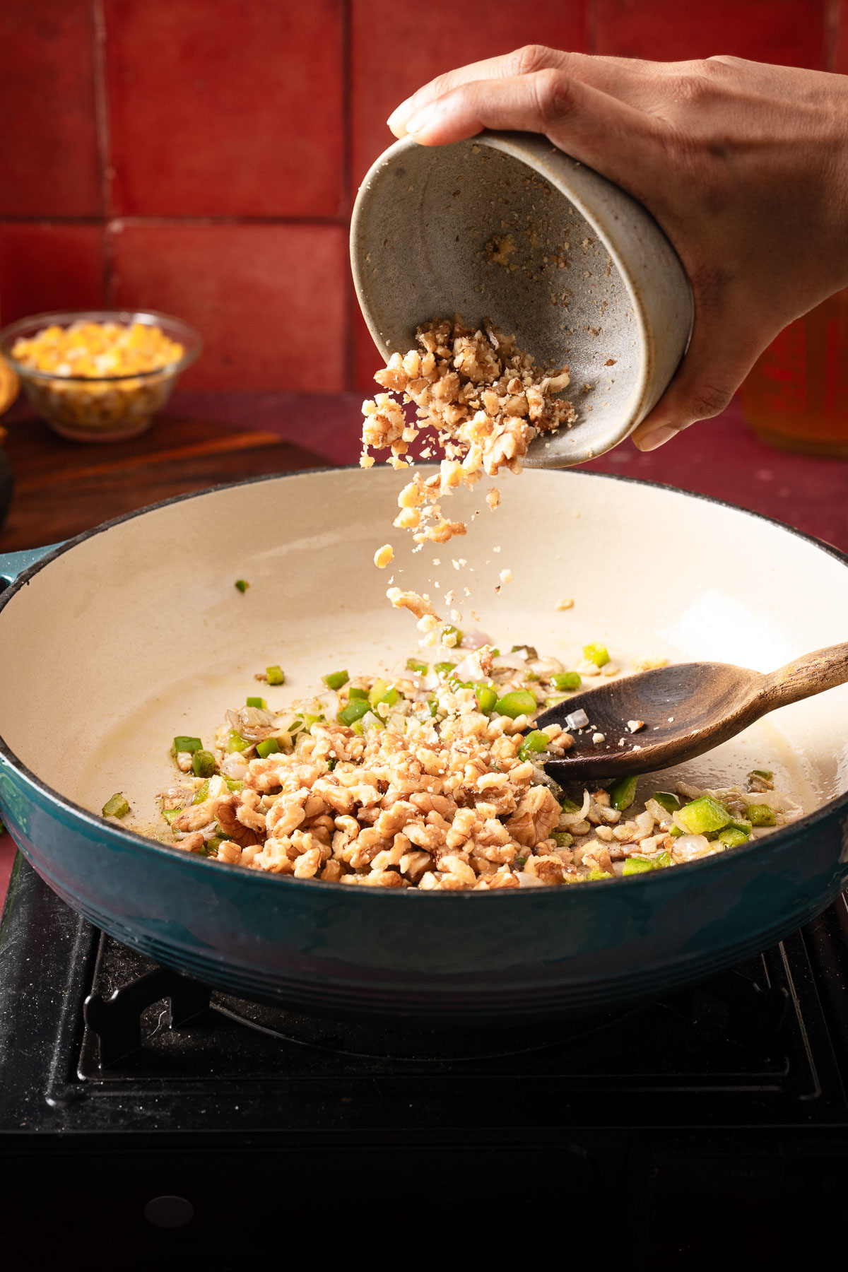 A person adding chopped walnuts to the sautéed vegetables