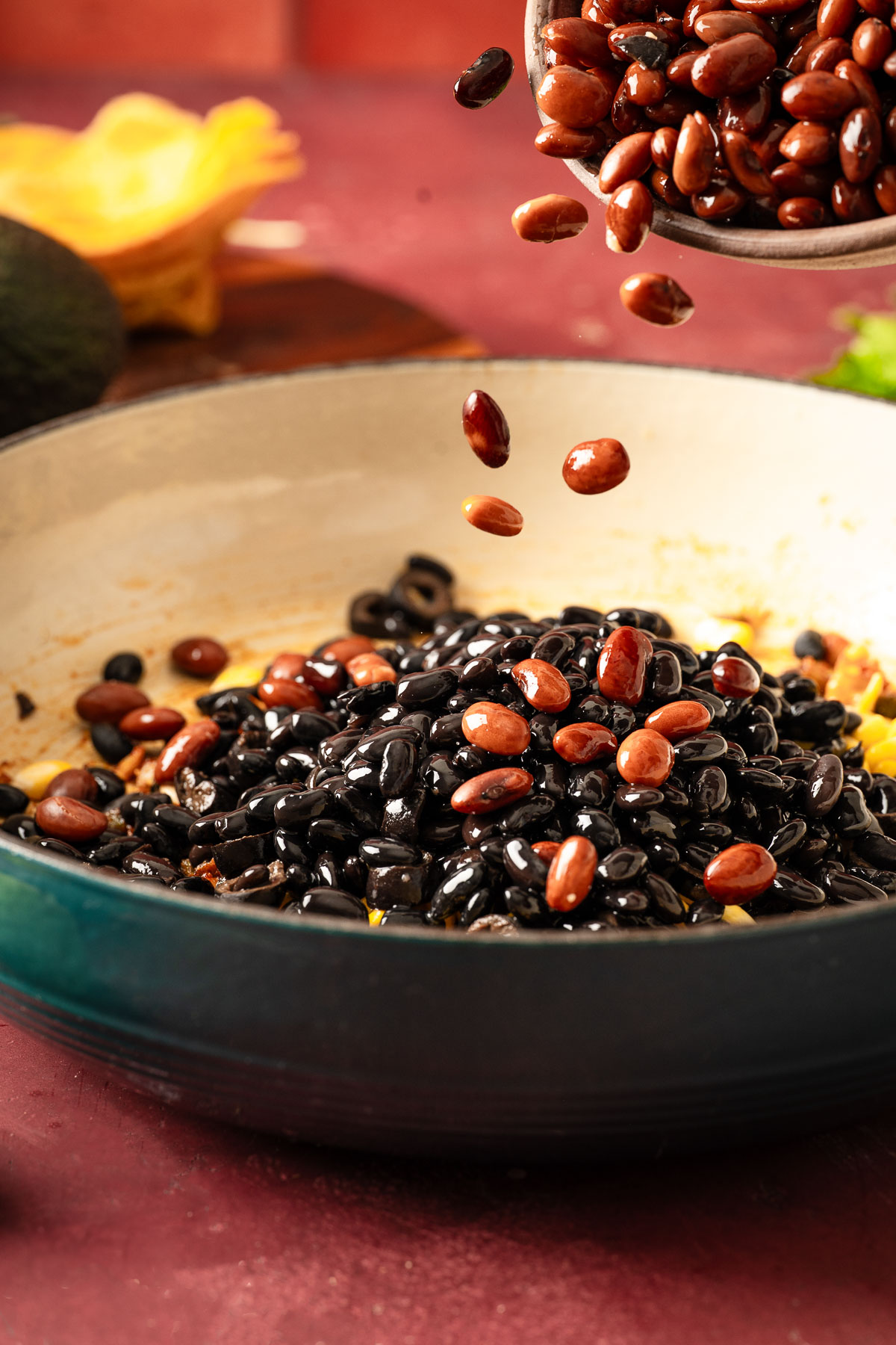 A mix of black and pinto beans being stirred into a skillet of seasoned vegetables