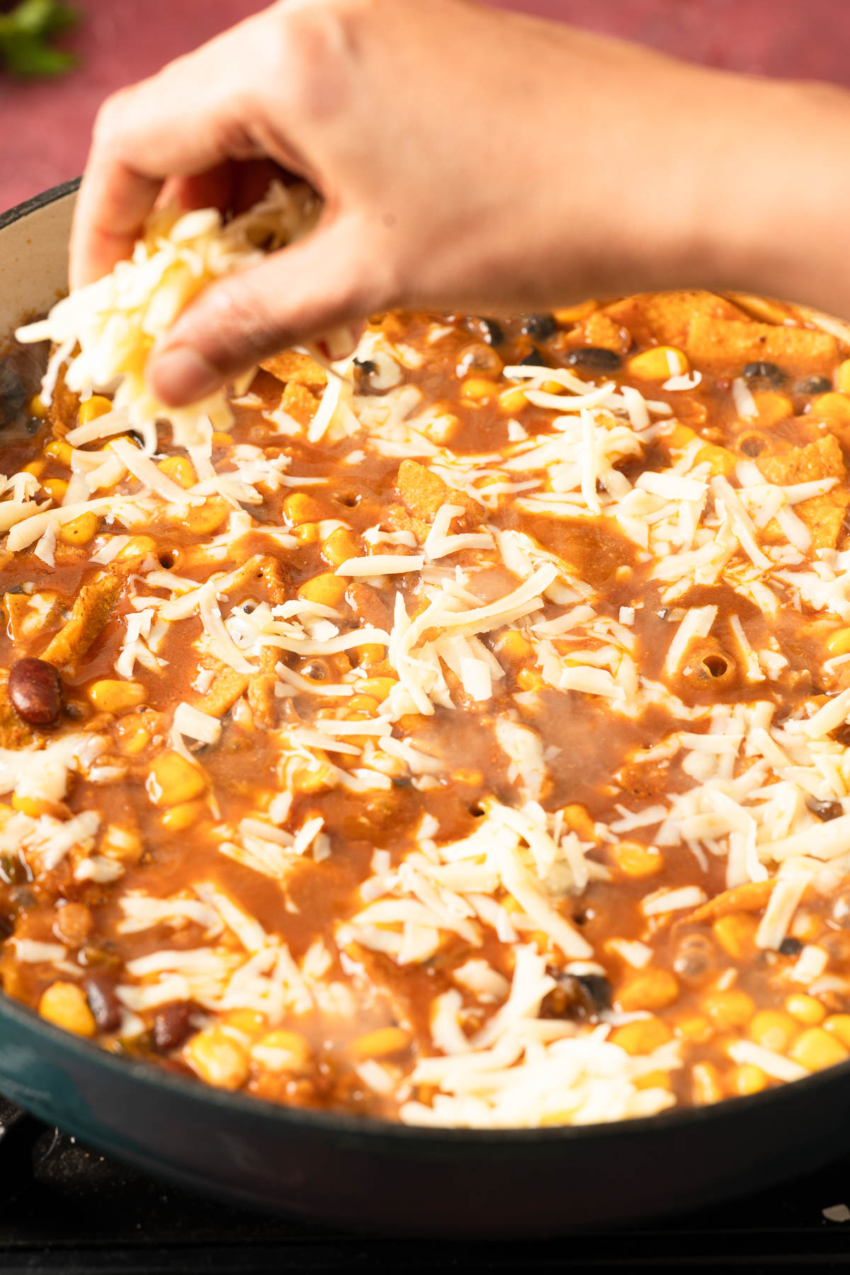 A person adding vegan shredded cheese over vegan enchiladas