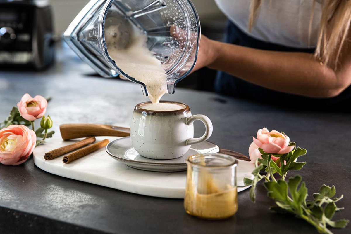 Creamy cinnamon dolce latte mixture being poured from a blender into a mug.